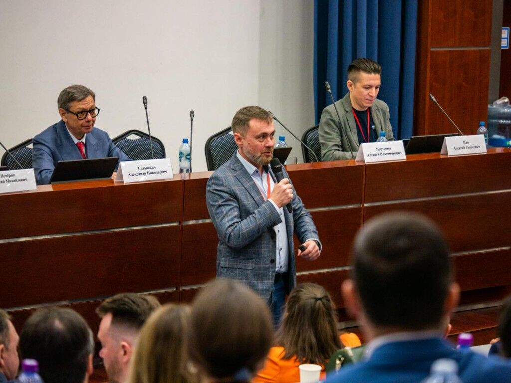 Спикер с микрофоном выступает перед залом на фоне президиума конференции АДР